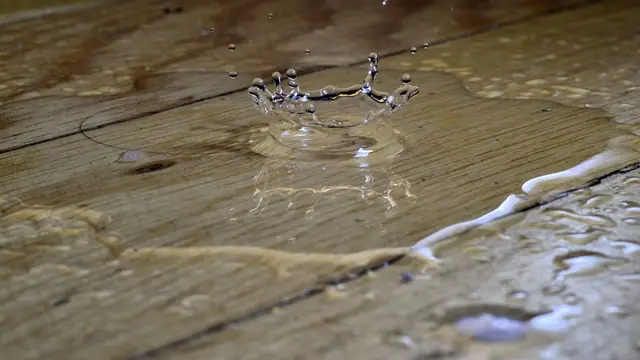 Water splashing on a wet hardwood plank floor with moisture pooling along the seams