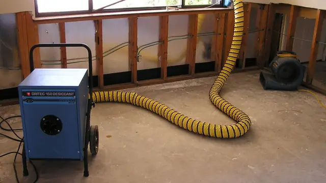 Desiccant dehumidifier with a yellow duct hose drying a room with open wall studs